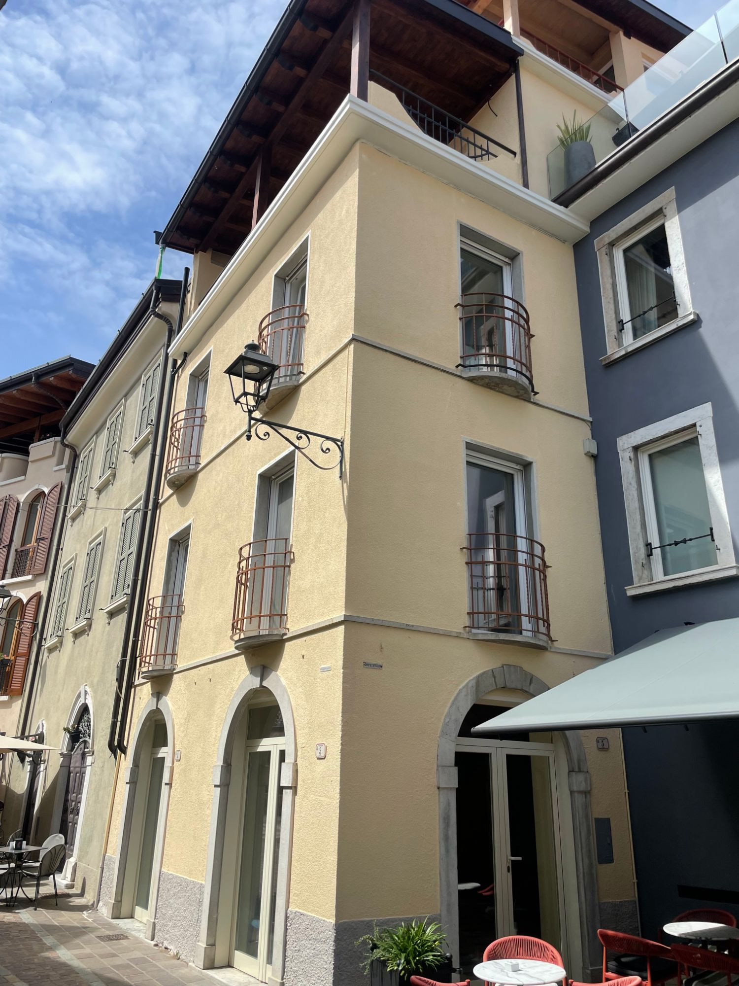 La casa finita vista dal vicolo: facciata gialla, balconi tondi con ringhiera in ferro, portali ad arco in pietra e lampione