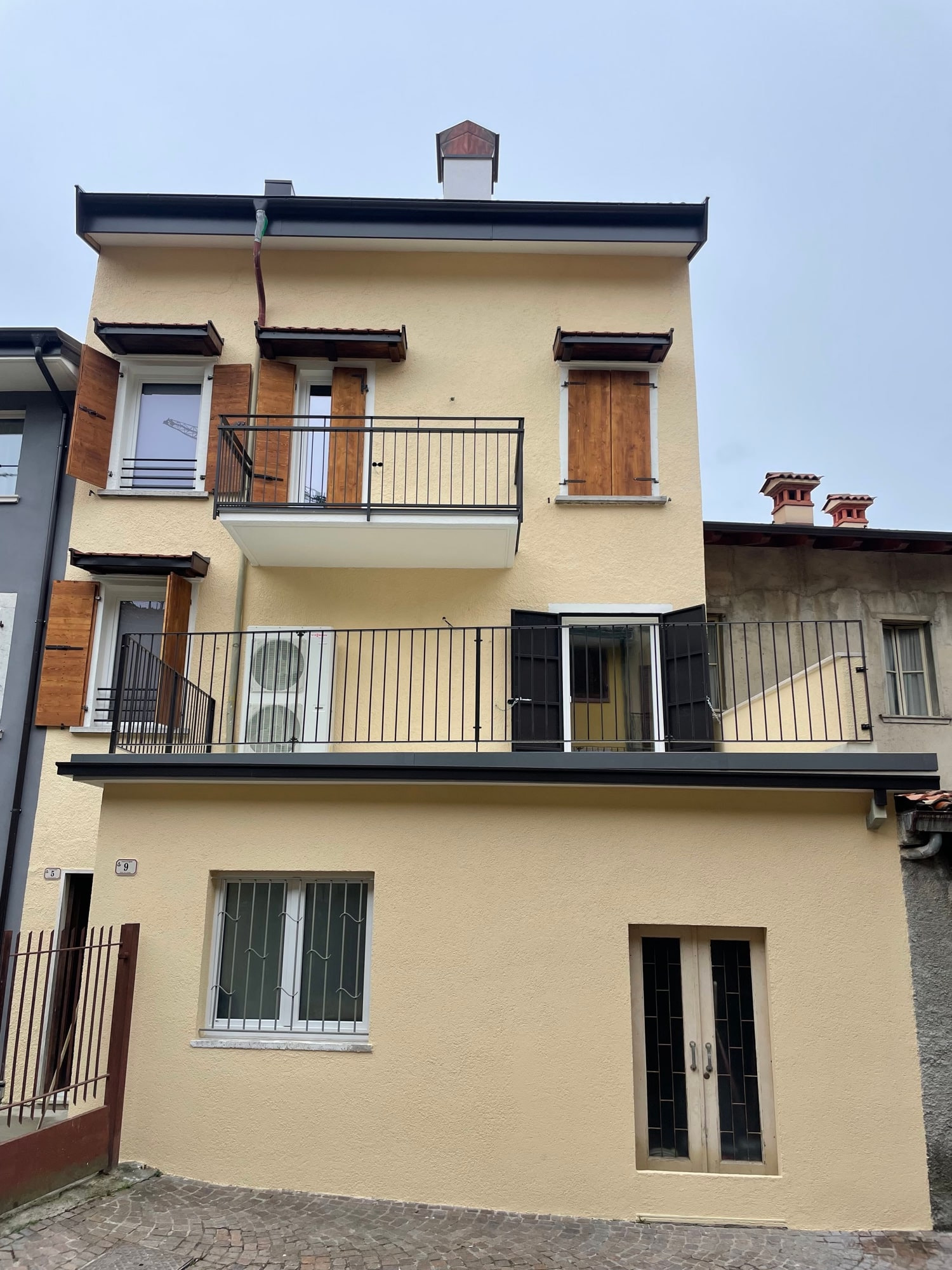 Casa ristrutturata: facciata gialla con scuri in legno, balconi con ringhiera in ferro e nuova grondaia
