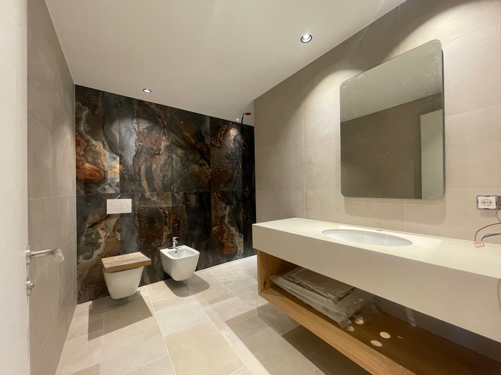 Bagno nuovo con parete in lastre effetto pietra, sanitari sospesi e lavabo su mobile in legno