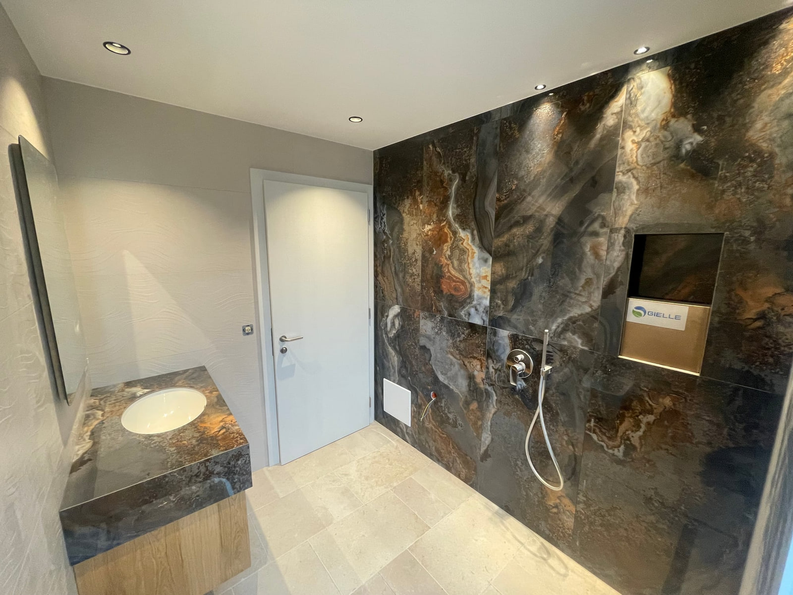 Bagno con parete in lastre effetto pietra scura, doccia a filo pavimento e lavabo su top in pietra con mobile in legno