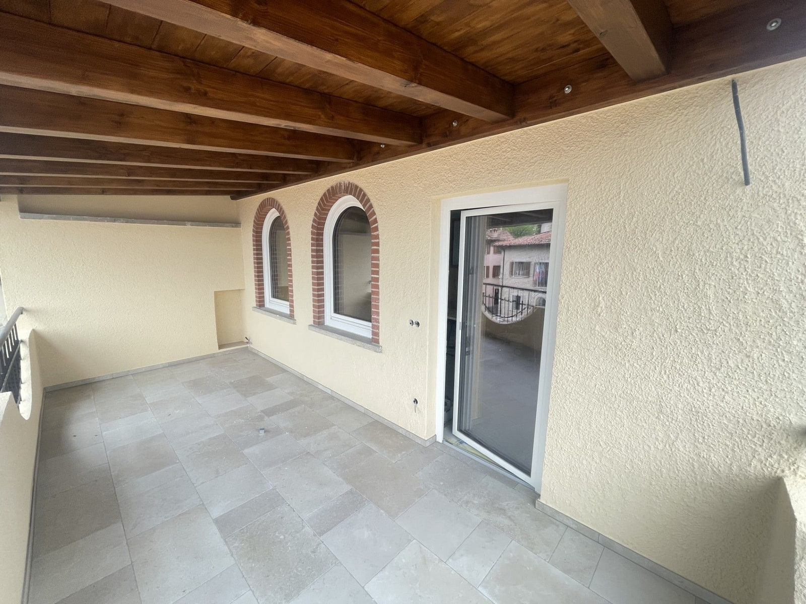 Terrazza coperta con soffitto in travi di legno, finestre ad arco con cornice in mattoni e portafinestra