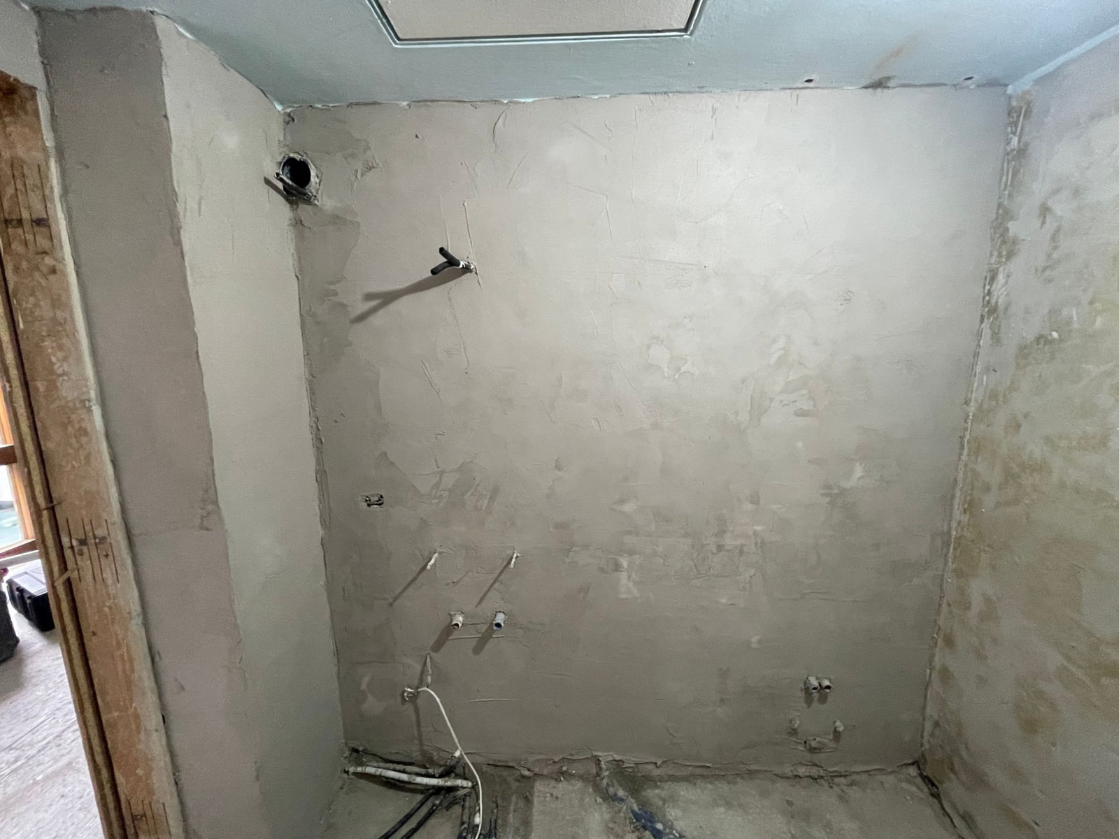 Parete del lavabo intonacata con gli attacchi di acqua e scarico